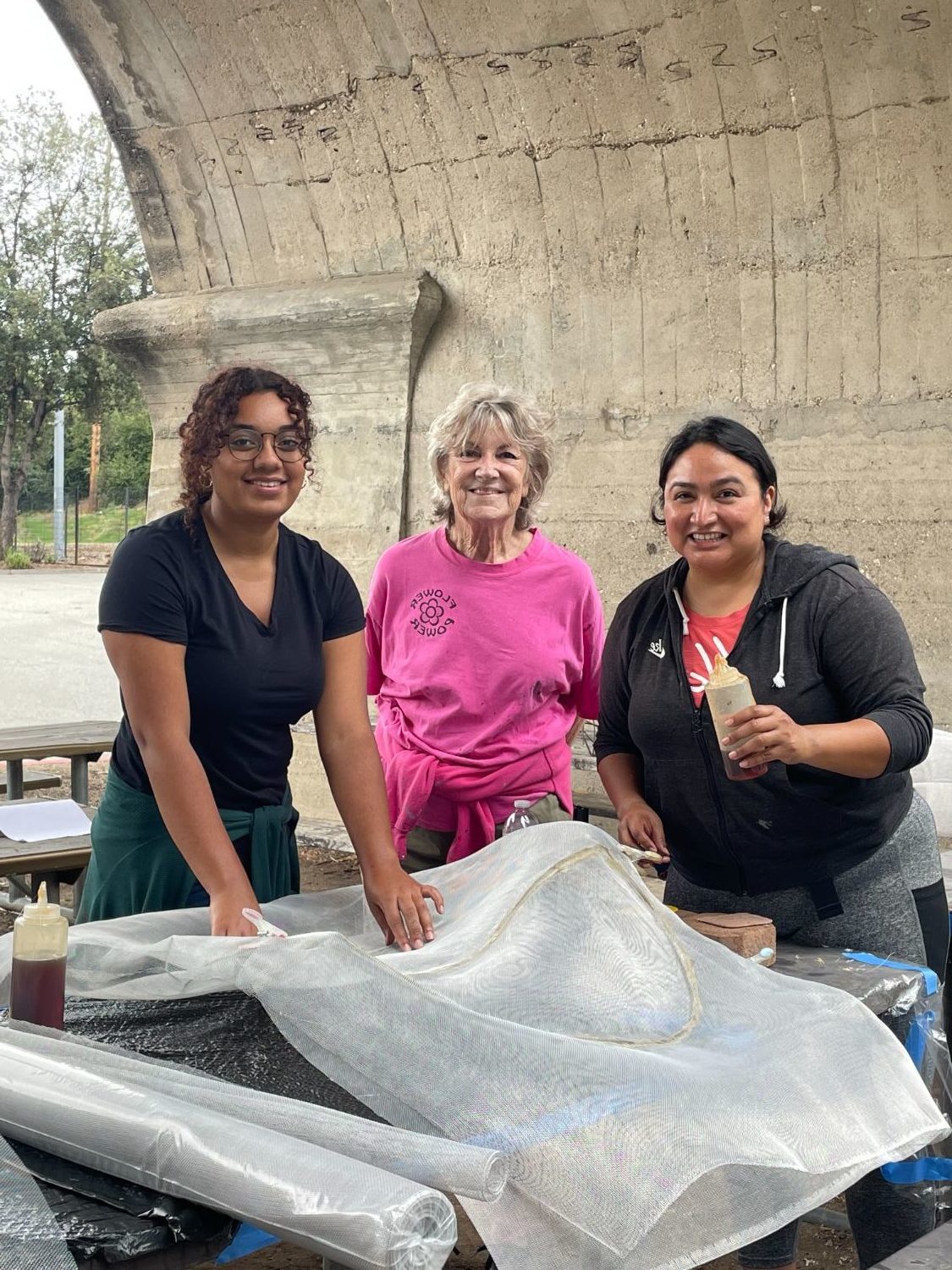 PHOTO: Sally Kilby | The South Pasadenan | Volunteers “screen” a sculpted metal flower, covering it with a window-screen-like material. This is the first layer in creating a feature that will appear on the 2024 South Pasadena float, “Boogie Fever.” L-R are Victoria Rea; Sharon Mitchell, volunteer assistant; and Alexandra Strong.